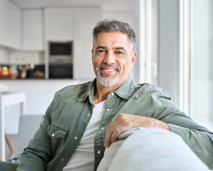 Middle-aged man smiling as he relaxes on a couch at home