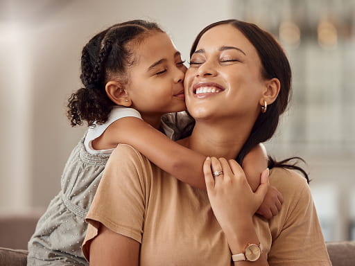 Young girl hugging and kissing her smiling mother at home